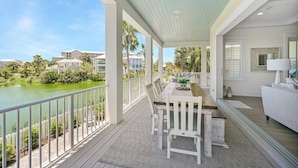 A covered outdoor area with a dining table and chairs, overlooking a body of water and greenery.