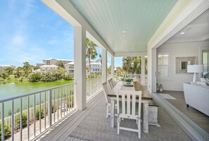 A covered outdoor area with a dining table and chairs, overlooking a body of water and greenery.