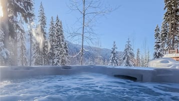 Relax in a serene hot tub surrounded by snow-covered trees and a majestic mountain.