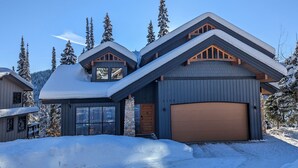 A modern two-story house with a garage, surrounded by snow-covered trees and a clear sky.