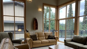 A spacious living room with large windows, a wooden coffee table, and leather sofas.