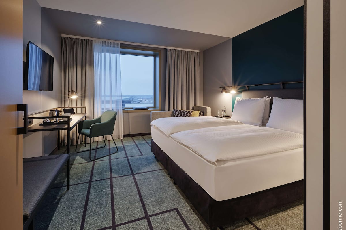 A hotel room with a large bed, a desk with a chair, a TV, and a window with curtains.