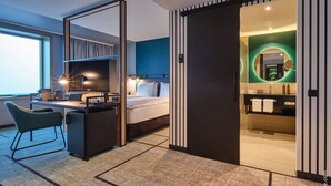 A modern hotel room with a desk, chair, bed, and a bathroom with a mirror and sink. - Dorint Hotel München/Garching (Garching)