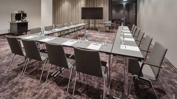 Ein Konferenzraum mit langem Tisch, Stühlen, einer Projektionsleinwand und einer Kaffeemaschine.