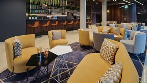 A modern lounge area with sofas and chairs, a bar with shelves of bottles, and a seating area with a patterned carpet. - Dorint Hotel München/Garching (Garching)