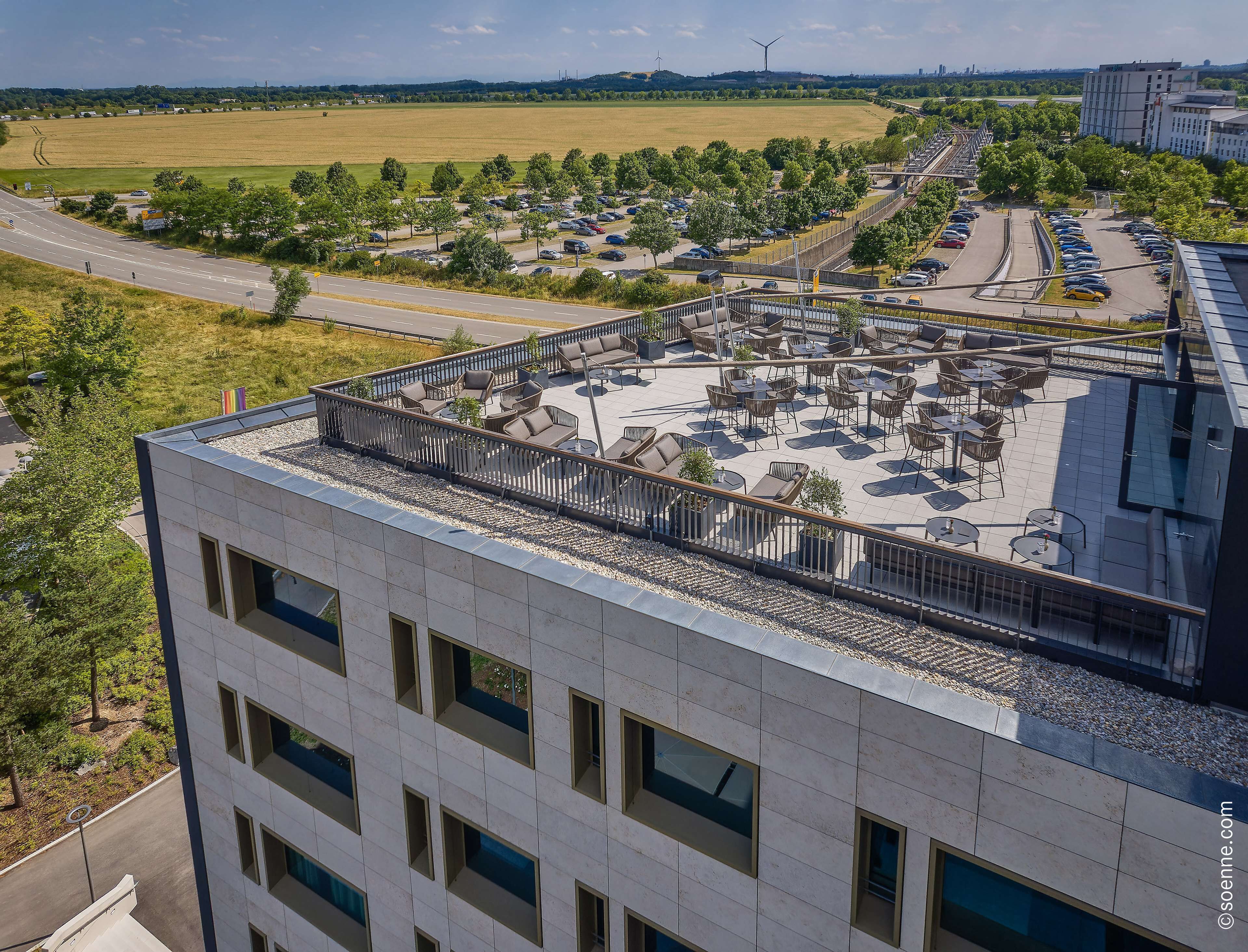 Eine Dachterrasse mit Sitzgelegenheiten im Freien und Blick auf einen Parkplatz und Felder.