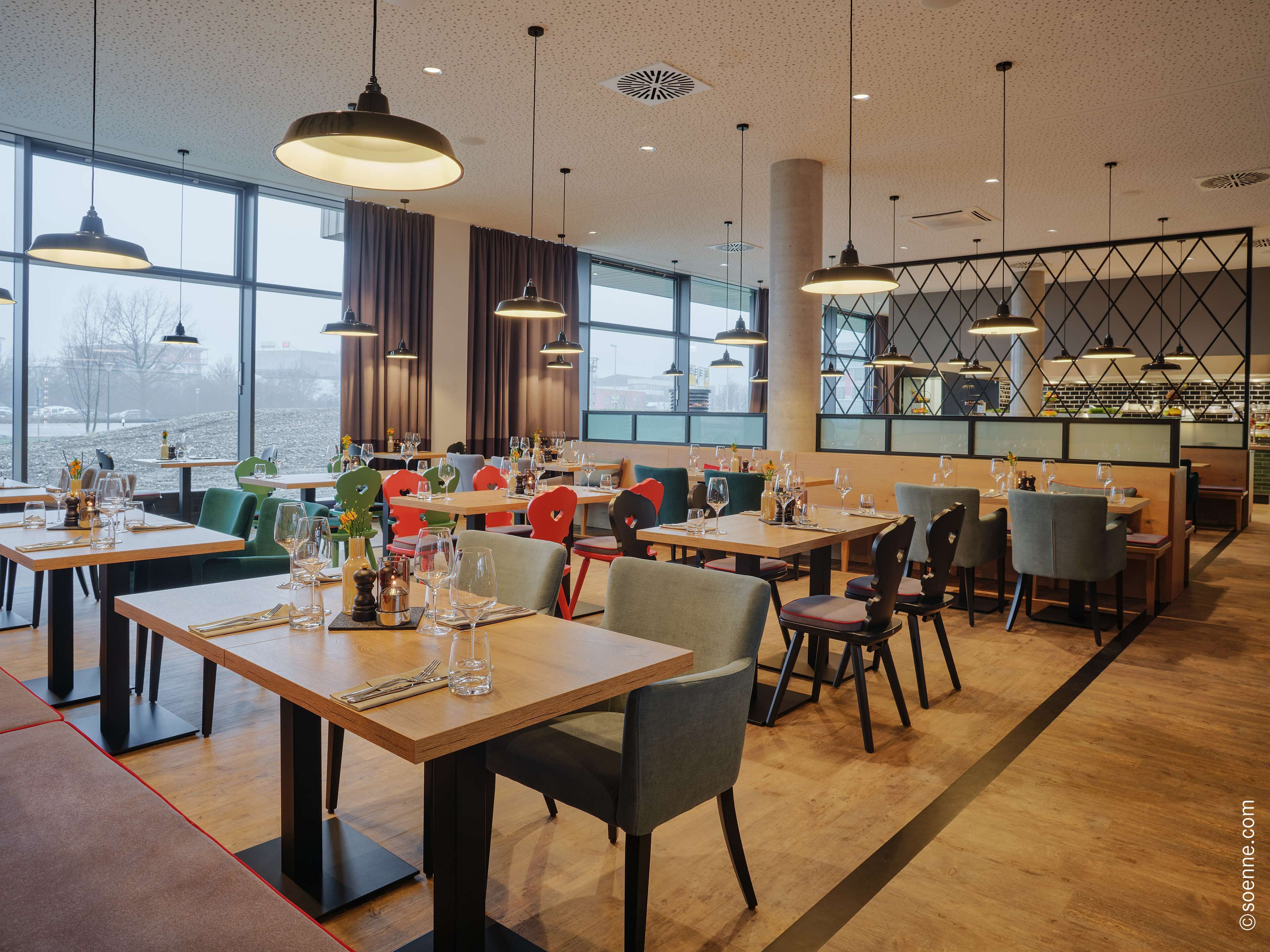 A modern restaurant with large windows, wooden tables, and colorful chairs.