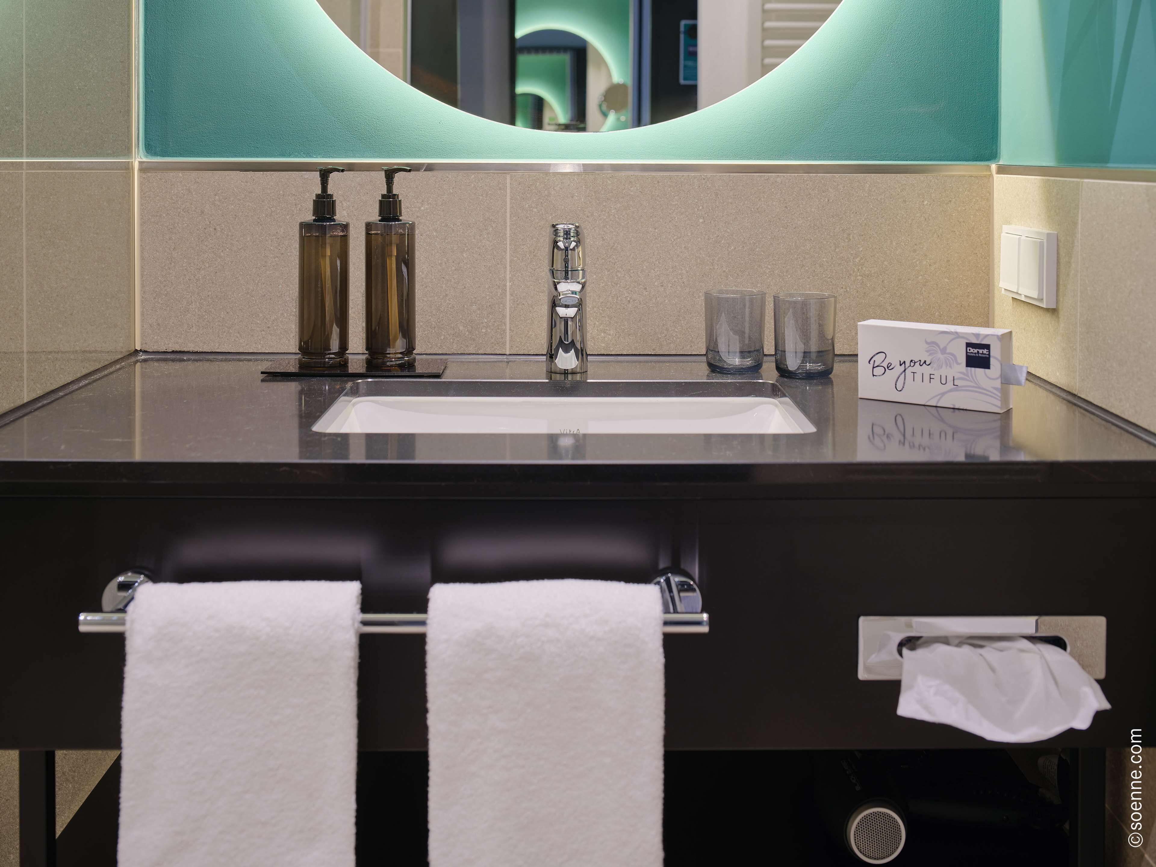 A modern bathroom with a large sink, two hand pumps, a mirror, and a towel rack.