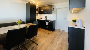 A modern kitchen with black cabinets, a wooden dining table, and chairs. - Vacation apartment with a view (Sankt Englmar)