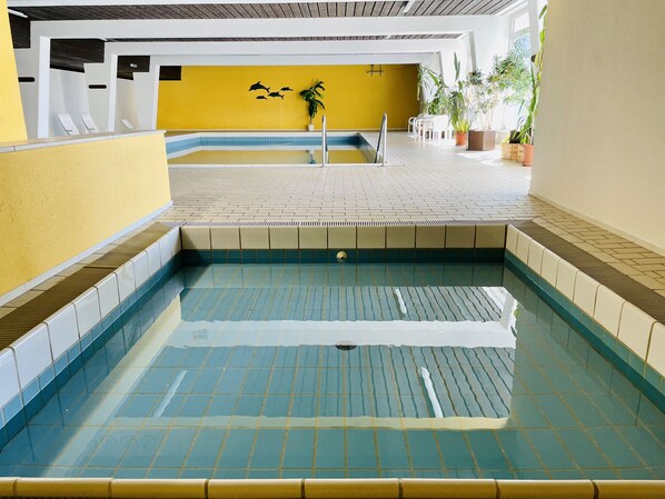 An indoor swimming pool with tiled walls and a yellow accent wall. - Vacation Apartment with a View (Sankt Englmar)