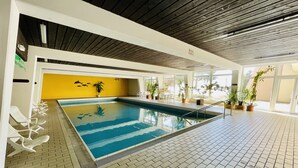 An indoor swimming pool with a tiled floor, a yellow wall, and several potted plants. - Vacation apartment with a view (Sankt Englmar)
