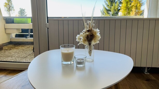 A white table with a candle and a glass vase with dried flowers. - Vacation apartment with a view (Sankt Englmar)