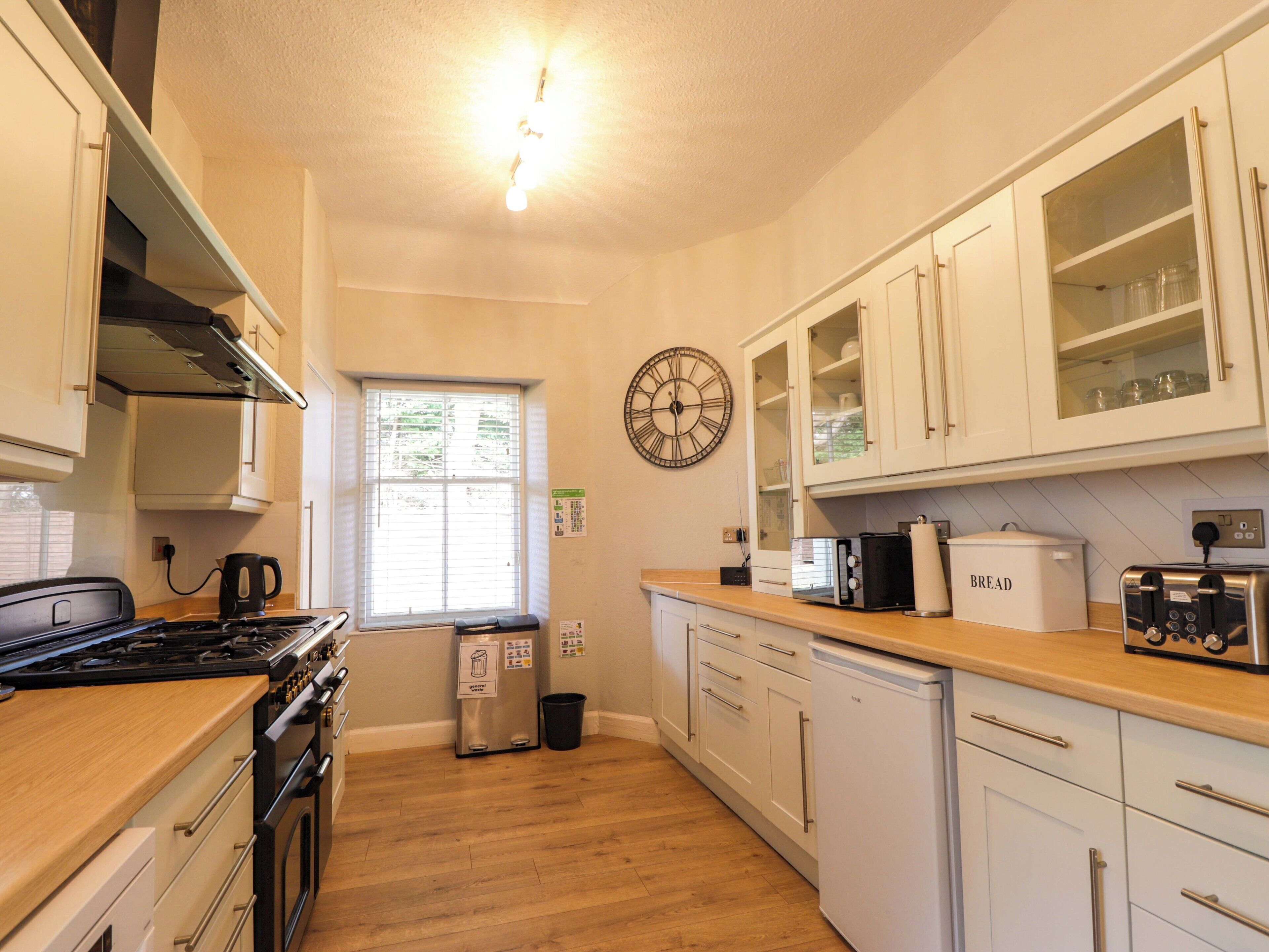 A kitchen with white cabinets, a stove, a toaster, and a clock on the wall.