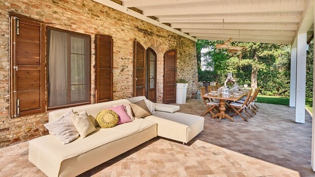 A covered patio with a brick wall, wooden shutters, a white sofa, and a dining table set for six. - San Martino, Certaldo, Florence and Chianti (Certaldo)