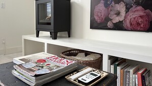 A living room with a black wood-burning stove, a magazine on a table, and a bookshelf with books. - Boutique Studio in the Heart of Charlevoix (Charlevoix)