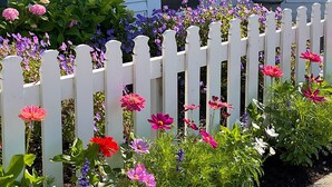 A white house with a number 107 on the door, surrounded by a white picket fence and colorful flowers. - Boutique Studio in the Heart of Charlevoix (Charlevoix)