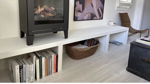 A modern living room with a black wood-burning stove, a white console table, a wicker basket, and a bookshelf filled with books. - Boutique Studio in the Heart of Charlevoix (Charlevoix)
