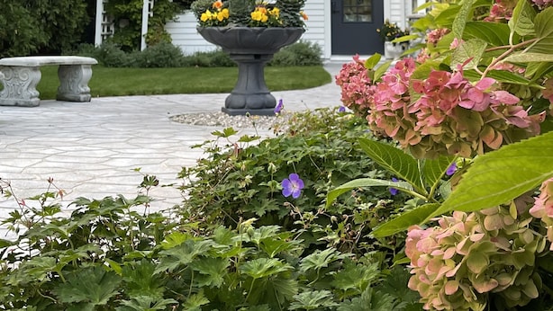 A white house with a stone chimney, a balcony with a railing, and a garden with a large planter and hydrangeas. - Boutique Studio in the Heart of Charlevoix (Charlevoix)