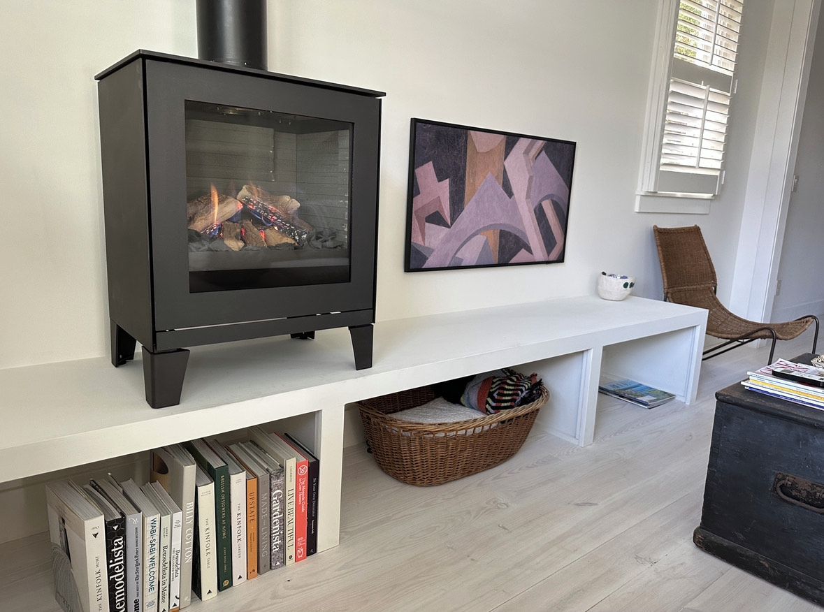 Een moderne woonkamer met een zwart houtvuur, een witte console tafel, een rieten mand en een boekenkast vol boeken.