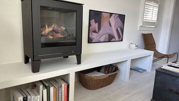 Een moderne woonkamer met een zwart houtvuur, een witte console tafel, een rieten mand en een boekenkast vol boeken.