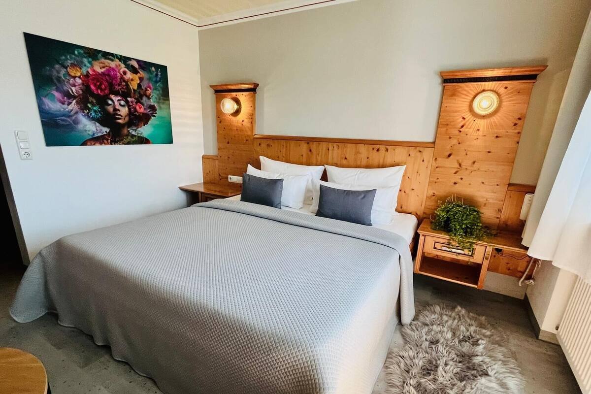 A modern bedroom with a large bed, wooden headboard, bedside tables with lamps, and a painting on the wall.