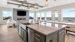 Una cocina moderna con una isla grande, un comedor con vistas al océano y una sala de estar con televisor.