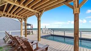 Una terraza de madera con piscina, vista a la playa y una bandera.