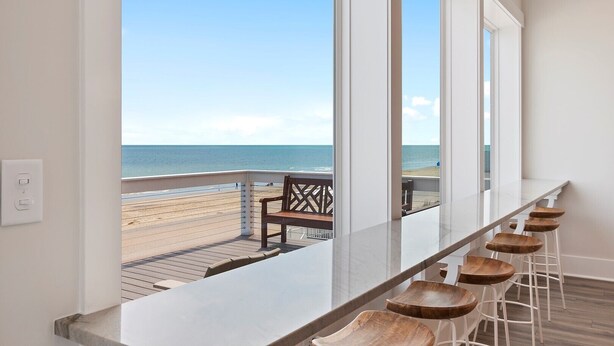 Un balcón con vista a la playa, un banco de madera y una zona de bar con taburetes.