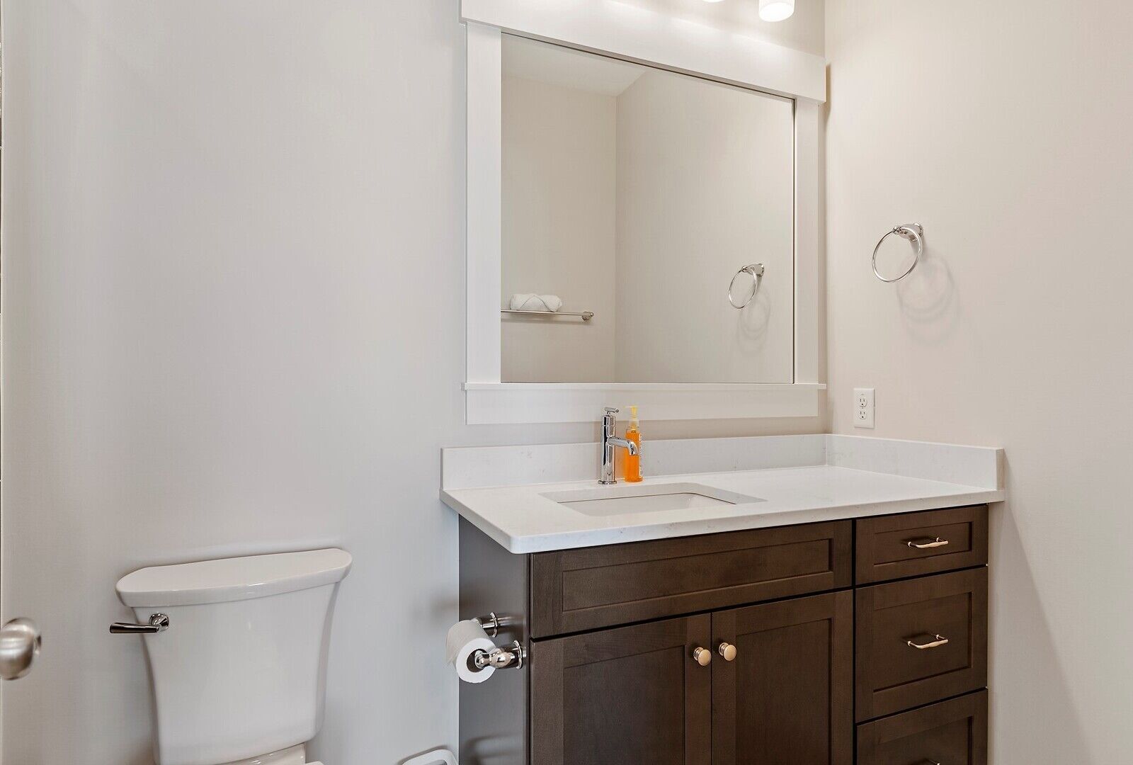 Een badkamer met een wit toilet, een wastafel met een spiegel erboven en een donker houten kastje met lades.