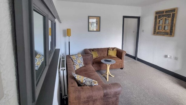 A living room with a brown sofa set, a small round table, and a framed picture on the wall. - Windsor Apartments (Dartford)