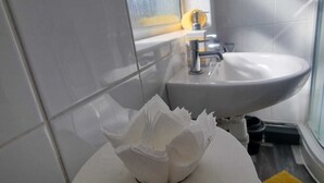 A bathroom with a white sink, a window, and a yellow bath mat. - Windsor Apartments (Dartford)