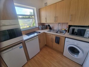 Een compacte keuken met een vaatwasser, magnetron, spoelbak en een raam voor natuurlijk licht.