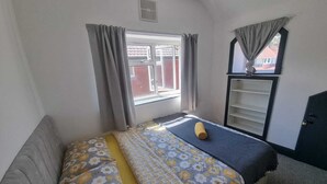 A small, simple room with a bed, a window, a wardrobe, and a radiator. - Windsor Apartments (Dartford)