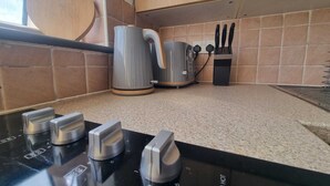 A kitchen with a gas stove, a kettle, and a knife block. - Windsor Apartments (Dartford)