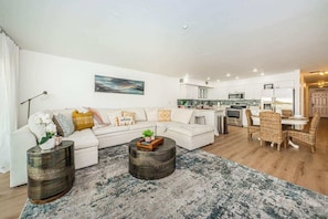 A modern living room with a sofa, coffee table, and a dining area with chairs.