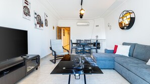 A modern living room with a flat-screen TV, a glass coffee table, a grey sofa, and a dining area with a table and chairs. - Superbe Appartement 2 Chambres Avec vue mer (Albufeira)