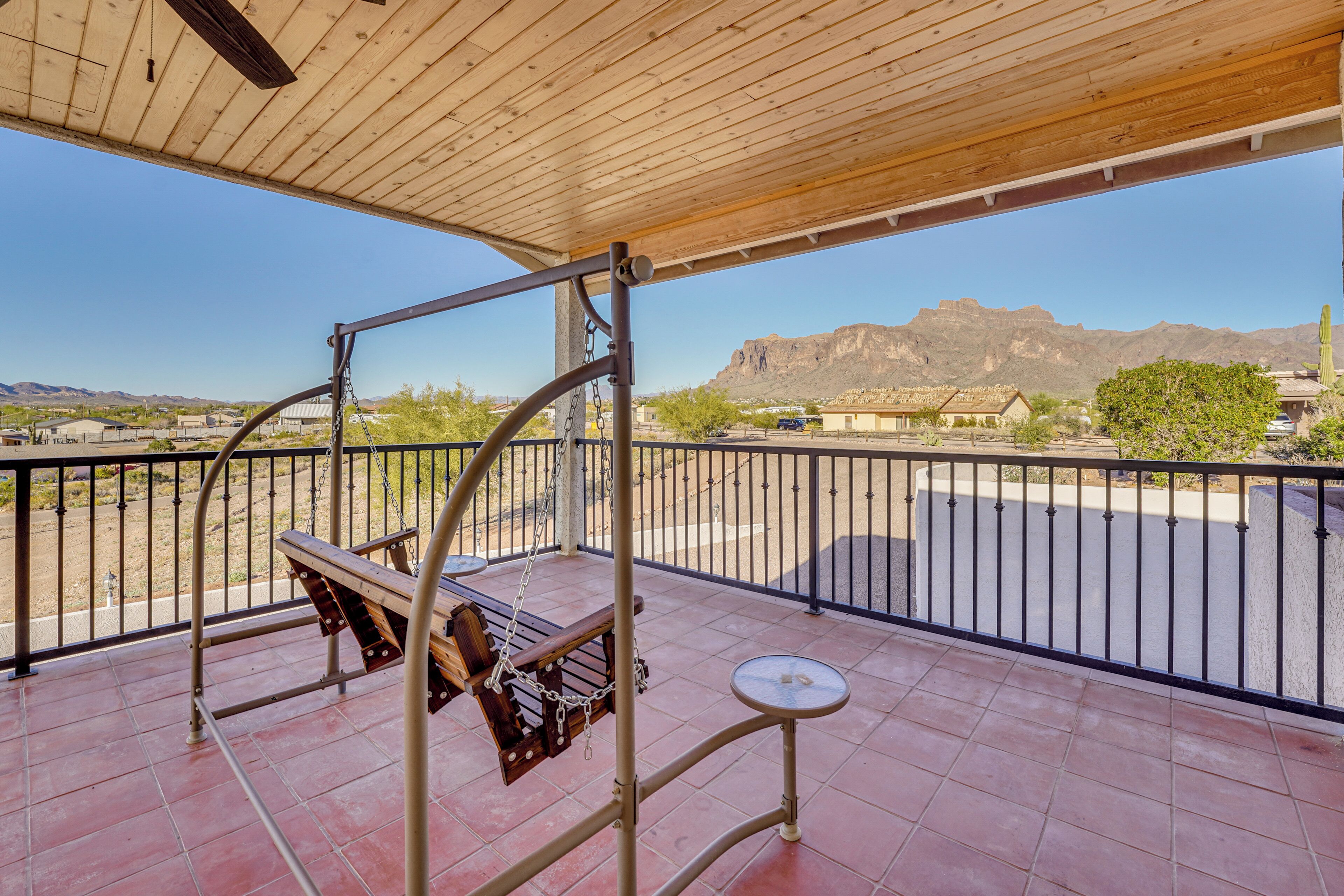 Ein Balkon mit einer Schaukel, einem kleinen Tisch und Blick auf Berge und Gebäude.