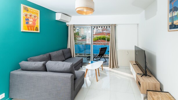 A modern living room with a grey sofa, a small white table, and a TV stand. - (012) L'armenonville à la plage (Antibes)