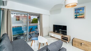 A modern living room with a sofa, TV, and a balcony with a pool. - (012) L'armenonville à la plage (Antibes)