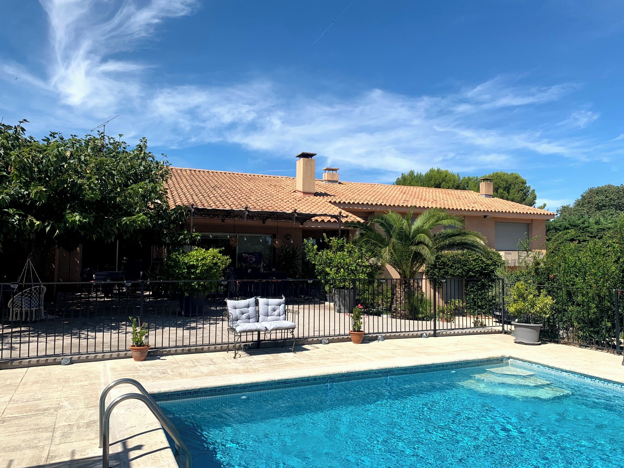 Une piscine dotée d’une terrasse carrelée, entourée d’une clôture et agrémentée de plantes en pot.