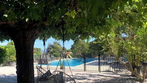 Ein Poolbereich mit einer Hängematte, einem umzäunten Pool und einem Baum, der Schatten spendet.