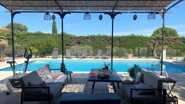 Ein Poolbereich mit Liegestühlen, einem Tisch und einer Pergola mit hängenden Lichterketten.