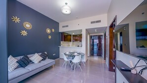 A modern living room with a grey sofa, a dining table with chairs, and decorative wall art. - Tanin - Unique Modern Apt with Stunning Canal View (Dubai)