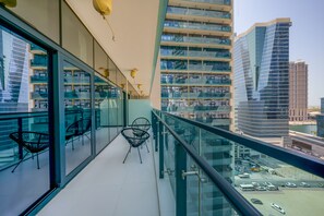 A balcony with glass railings, black chairs, and a view of a parking lot and buildings. - Tanin - Unique Modern Apt with Stunning Canal View (Dubai)