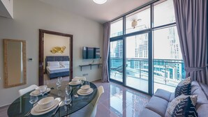 A modern living room with a dining area, large windows, a sofa, and a TV. - Tanin - Unique Modern Apt with Stunning Canal View (Dubai)