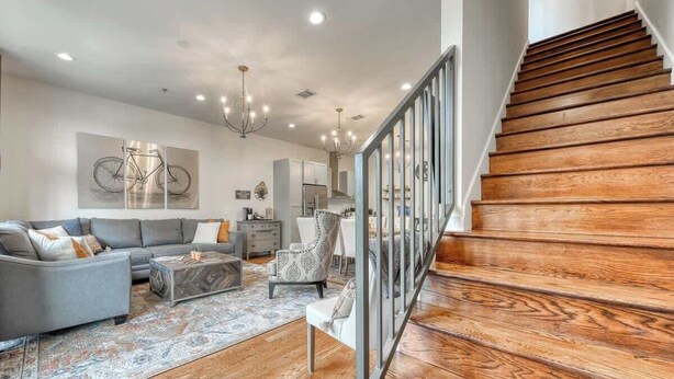 Un salon spacieux avec un canapé gris, un fauteuil à motifs et une table basse. Un escalier avec des marches en bois et une rampe en métal mène à l’étage supérieur.