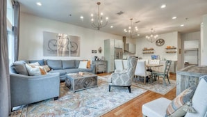 A spacious living room with a grey sofa, patterned armchair, and a coffee table. - Steps to Pearl - Two Townhomes - Sleeps 22 (San Antonio)
