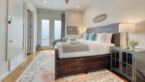 A bedroom with a bed, a ceiling fan, a nightstand, a lamp, and a view of the outdoors. - Steps to Pearl - Two Townhomes - Sleeps 22 (San Antonio)
