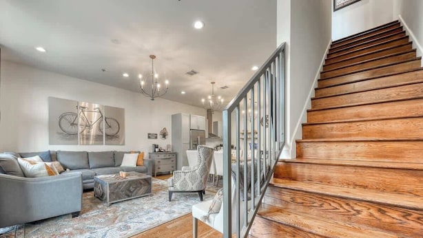 A spacious living room with a grey sofa, a patterned armchair, and a wooden staircase. - Steps to Pearl - Two Townhomes - Sleeps 22 (San Antonio)