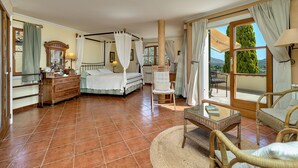 A bedroom with a four-poster bed, a sitting area with wicker furniture, and a view through a large window. - Townhouse with pool and mountain views, just 5 minutes from Pollensa downtown  (Pollensa)